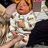 baby, sleeping, headband, yellow_bow, onesie, cookie_pattern, infant, hand, tattoo, person, indoor, clothing, fabric, bedroom, casual, relaxation, cute, newborn, comfort, soft
