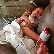 Zayla is registered to the contest to win money with this photo: newborn, baby, infant, pacifier, blanket, hospital, medical_sensor, couch, arm, adult, resting, sleeping, skin, foot, hand, closeup, indoor, person, comfort, care