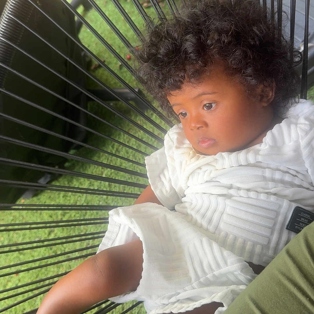 Djulïyan a rejoint le concours — aidez-le/la à gagner de superbes lots ! barefoot, casual, chair, child, contemplative, curly_hair, cute, daylight, fashion, grass, legs, outdoor, person, portrait, relaxing, resting, seat, toddler, white_clothing, wire_frame