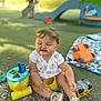 bucket, casual_clothing, child, childhood, daylight, grass, happy, orange_car, outdoor, park, pebbles, person, play, playground, smile, sneakers, summer, toddler, toy, toy_truck