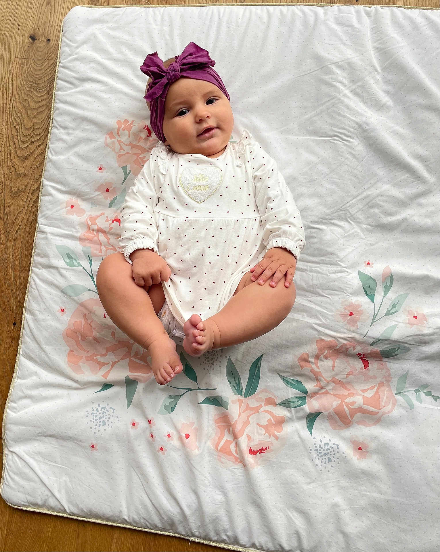 Lucie participe au concours pour gagner de l'argent avec cette photo : baby, infant, headband, purple, bow, blanket, floral_pattern, wooden_floor, white_clothing, cute, child, lying_down, soft_lighting, indoors, small_hands, small_feet, portrait, adorable, calm, looking_at_camera