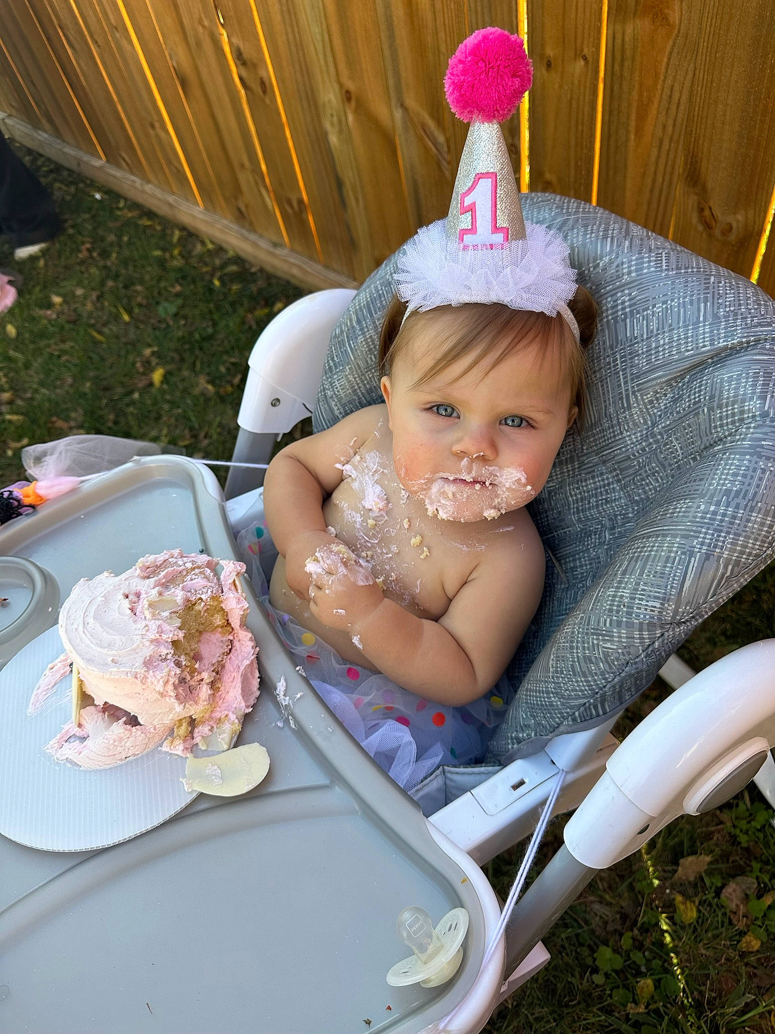 Remington is registered to the contest to win money with this photo: baby, baby_toddler_clothing, chair, child, costume_hat, event, fashion_accessory, food, fun, grass, happy, headpiece, party_hat, person, pink, plate, sitting, smile, sweetness, tableware