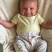 Malik is registered to the contest to win money with this photo: baby, infant, smile, face, clothing, pajamas, blanket, fabric, person, cute, child, sitting, soft, texture, indoors, winnie_the_pooh, pattern, light, happy, relaxed