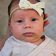 Elena is registered to the contest to win money with this photo: baby, newborn, infant, headband, bow, eyes, face, hand, adult_hand, clothing, swaddle, blanket, portrait, close_up, skin, lips, hair, expression, neutral_background, soft_lighting