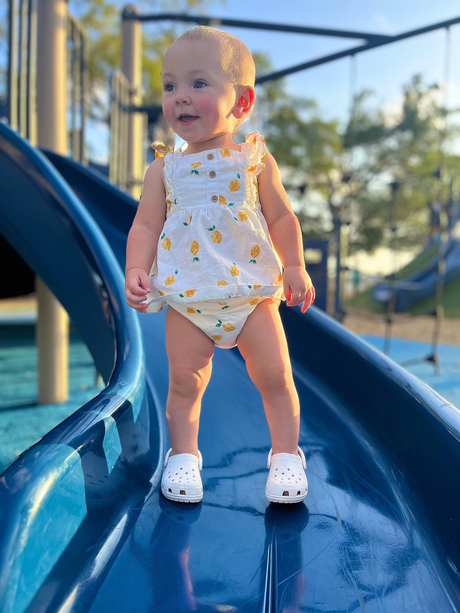 Allison joined the competition — help win amazing prizes! baby, baby_toddler_clothing, blue, child, chute, city, electric_blue, fun, happy, human_leg, leisure, outdoor_play_equipment, person, playground, recreation, sitting, sky, smile, summer, thigh