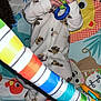 baby, infant, toy, play_mat, onesie, rattle, colorful, striped_toy, hardwood_floor, flash, red_eye, lying_down, hands, wide_eyes, teething_toy, cartoon_pattern, play_gym, cute, cozy, pajamas