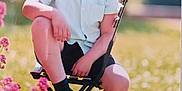 Logan a rejoint le concours — aidez-le/la à gagner de superbes lots ! black_shoes, bow_tie, boy, casual_clothing, chair, child, daylight, flowers, garden, grass, greenery, happy, nature, outdoor, portrait, shirt, shorts, sitting, smiling, sunlight