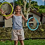 child, girl, smiling, outdoor, grass, hoops, playing, summer, casual_clothing, shorts, tank_top, happy, daylight, trees, stone_wall, house, nature, recreation, fun, leisure
