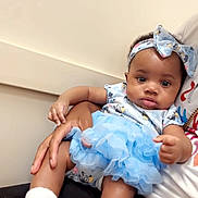 Josie is registered to the contest to win money with this photo: baby, child, infant, blue_skirt, headband, socks, person, hand, sitting, cute, portrait, indoor, clothing, skin, face, expression, holding, lap, young, adorable