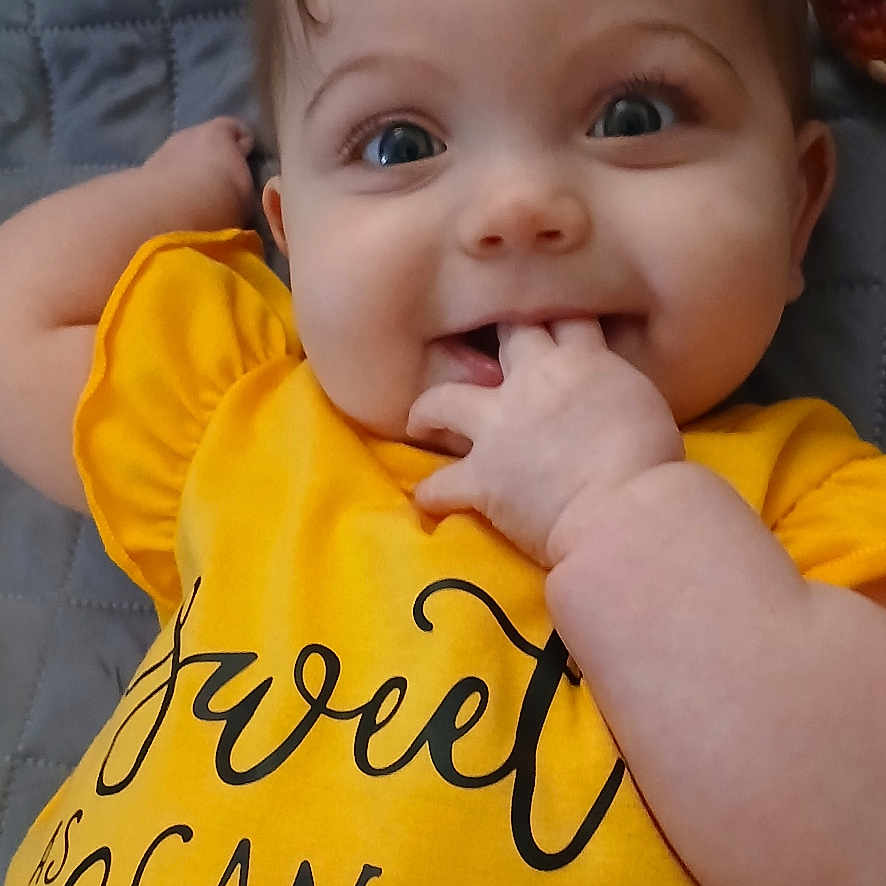 Blakely joined the competition — help win amazing prizes! adorable, baby, baby_girl, bee_graphic, blue_eyes, casual_clothing, child, closeup, cute, face, hand_in_mouth, happy, indoor, infant, lying_down, portrait, quilted_blanket, smiling, soft_lighting, yellow_shirt