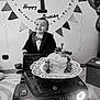baby, balloons, banner, birthday, black_and_white, bow_tie, cake, car, celebration, child, clothing, face, happy, indoor, luxury_toy, party_decor, portrait, smiling, toddler, toy_car