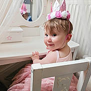 Isabella is registered to the contest to win money with this photo: toddler, child, pink_crown, tutu_dress, white_chair, vanity_mirror, curtains, smile, indoor, furniture, face, person, cute, birthday_hat, playroom, pink, dress, hair, baby, happy