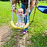 adult, baby, blue_swing, child, grass, grass_field, hand, holding_hands, jeans, long_hair, outdoor, park, person, playground, rope, shoes, sunny, swing, tshirt, yellow_swing