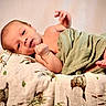 baby, blanket, child, cute, face, green_cloth, indoors, infant, lying_down, newborn, patterned_blanket, peaceful, portrait, resting, skin, small_feet, small_hands, soft_lighting, wooden_surface, wrapped
