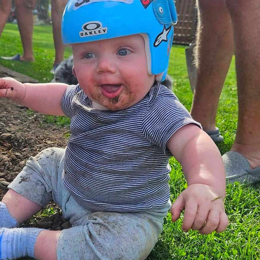 Otis joined the competition — help win amazing prizes! baby, helmet, grass, dirt, smiling, outdoor, child, person, blue_helmet, casual_clothing, sunlight, toy_wheel, happy, nature, playtime, legs, adult, greenery, daylight, fun