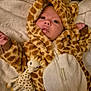 baby, infant, giraffe_toy, hooded_outfit, blanket, plush, spots_pattern, cozy, newborn, lying_down, cute, wide_eyes, onesie, zipper, hand, soft_texture, nursery, teether, animal_print, portrait