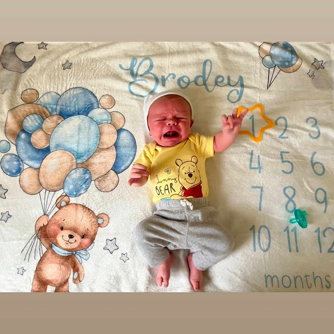 Brodey is registered to the contest to win money with this photo: baby, balloons, bear, child, crying, cute, expression, gray_pants, headwear, illustration, infant, lying_down, milestone_blanket, months, numbers, pacifier, pastel_colors, soft_texture, winnie_the_pooh, yellow_shirt