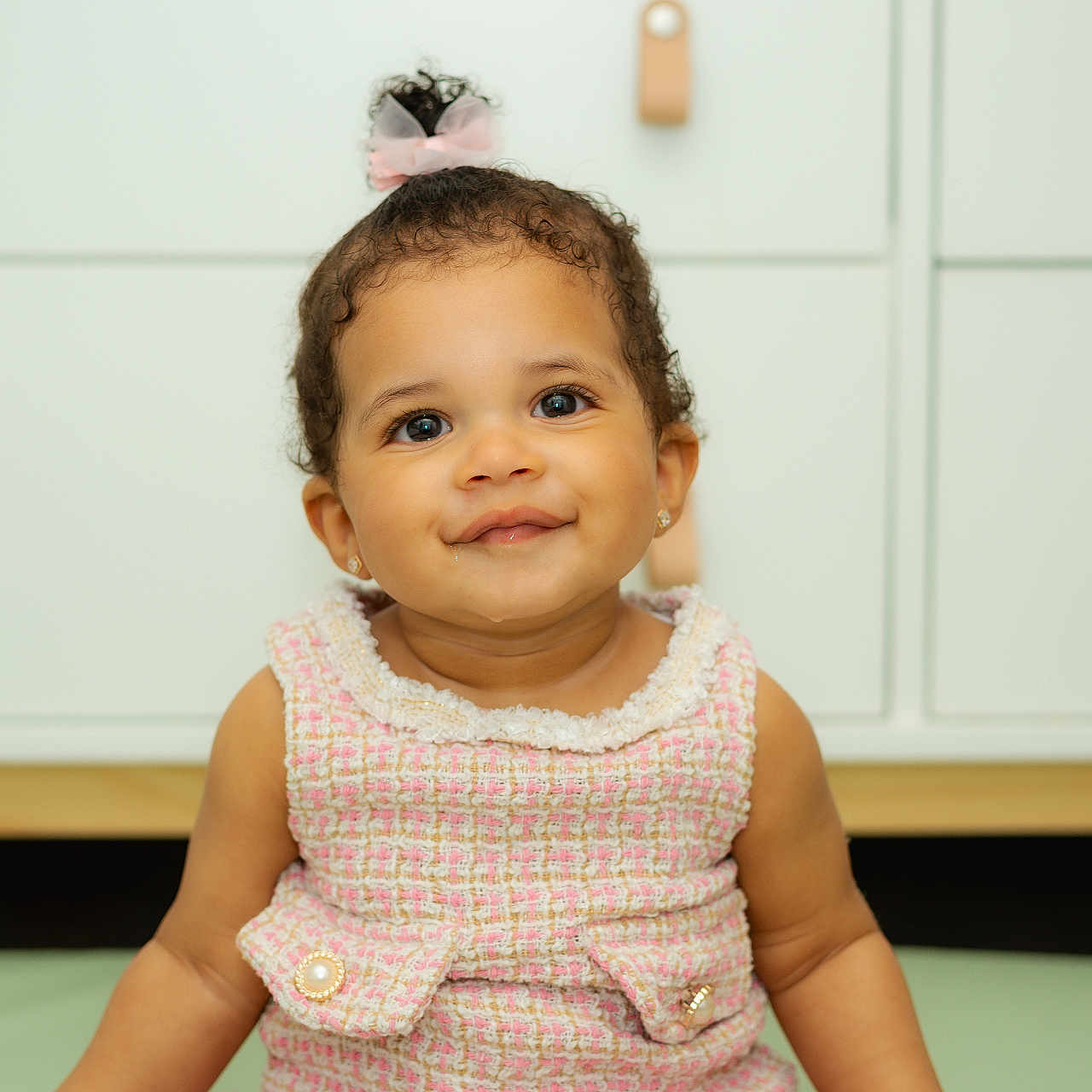 Briella joined the competition — help win amazing prizes! baby, background, button, cabinet, child, curly_hair, cute, dress, earrings, eyes, face, furniture, happy, indoors, pink_bow, portrait, sitting, skin, smile, toddler