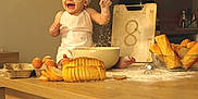 Manaël a rejoint le concours — aidez-le/la à gagner de superbes lots ! apron, baby, baking, bowl, bread, chef_hat, child, cooking, counter, eggs, flour, food, happy, indoor, kitchen, messy, person, playful, smile, wooden_table