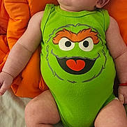 Idenshi joined the competition — help win amazing prizes! baby, infant, onesie, green_clothing, cartoon_face, orange_cushion, baby_socks, smiling, lying_down, cute, child, indoor, playful, happy, young_child, red_bracelet, skin, head, face, expression