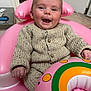 baby, infant, smiling, pink_inflatable, float_ring, knitted_sweater, buttons, hand, fist, face, eyes, mouth_open, rosy_cheeks, baby_seat, indoor, tiled_floor, doorway, toy, portrait, happy