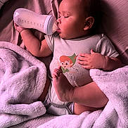 Elijah joined the competition — help win amazing prizes! baby, bottle, blanket, sleeping, infant, onesie, cartoon_print, bed, cozy, child, cute, peaceful, soft_texture, resting, small_hand, foot, pink_tone, nursery, indoors, portrait