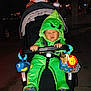 baby, child, stroller, costume, green, hood, plush_toy, night, outdoor, face, scrunched_face, hand, footwear, toy, person, expression, graco, cute, infant, clothing