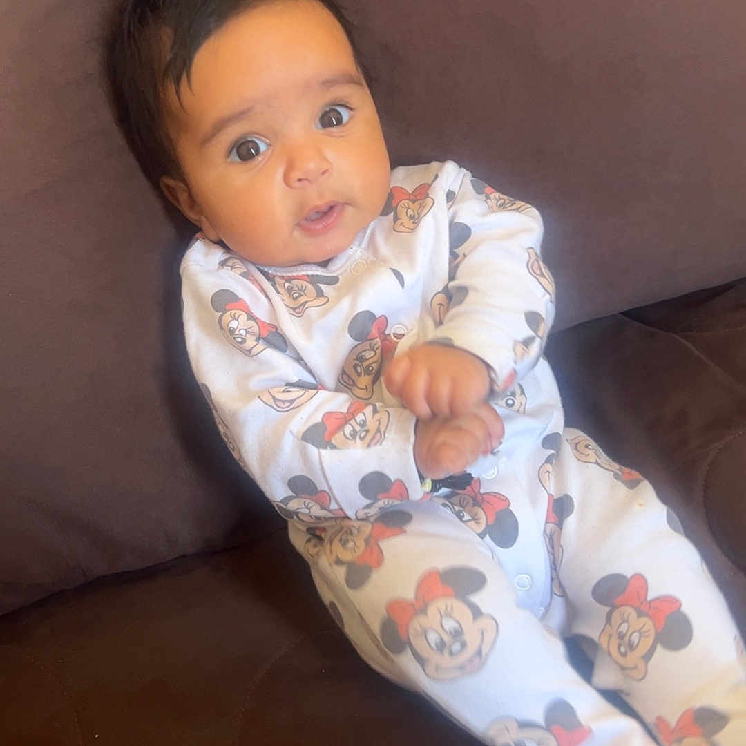 Djanna a rejoint le concours — aidez-le/la à gagner de superbes lots ! baby, brown, child, clothing, comfortable, couch, cute, expression, face, furniture, hands, indoors, infant, mickey_mouse, minnie_mouse, onesie, person, portrait, sitting, young