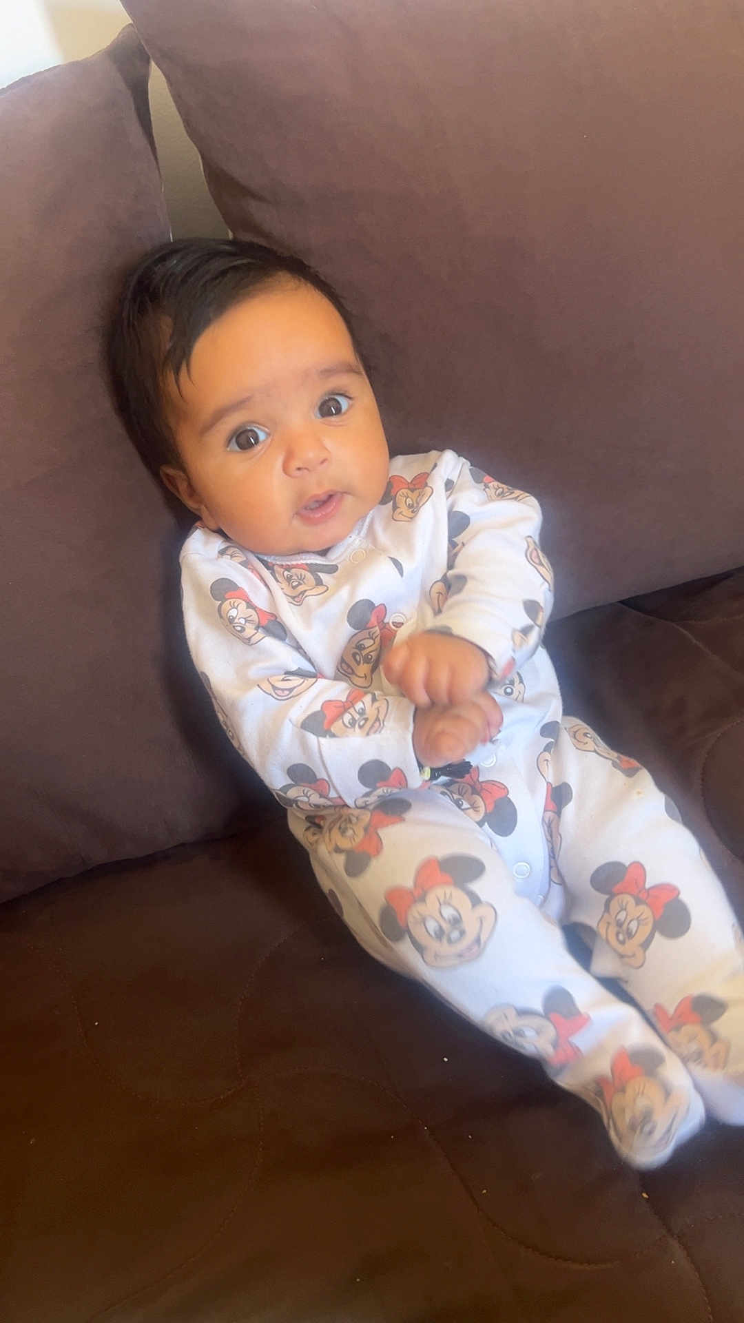 Djanna a rejoint le concours — aidez-le/la à gagner de superbes lots ! baby, infant, child, onesie, mickey_mouse, minnie_mouse, clothing, couch, brown, furniture, indoors, person, cute, face, hands, expression, sitting, comfortable, young, portrait