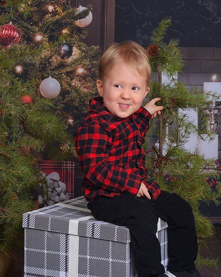 Lucas joined the competition — help win amazing prizes! christmas, christmas_decoration, christmas_eve, christmas_ornament, christmas_tree, event, facial_expression, fun, holiday, joy, ornament, pattern, person, pet_supply, plaid, plant, sitting, sleeve, smile, tartan