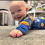 Bohdi joined the competition — help win amazing prizes! baby, child, crawling, carpet, onesie, space_theme, smiling, indoor, toy, trash_can, floor, hand, face, head, person, blue_clothing, orange_clothing, home, happy, infant