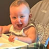 baby, child, high_chair, smiling, happy, indoor, clothing, face, arm, furniture, plaid, person, portrait, infant, table, cheerful, young, cute, skin, light