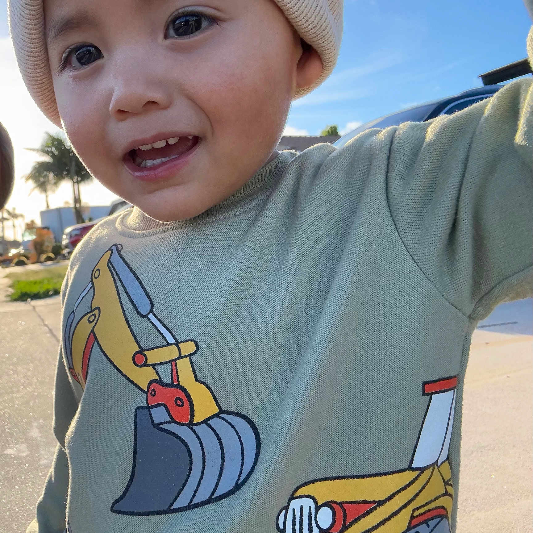 Noah is registered to the contest to win money with this photo: child, smiling, face, hat, beanie, sweater, excavator_print, outdoor, sunny, blue_sky, palm_tree, daylight, happy, young_child, casual_clothing, closeup, person, portrait, cute, playful