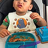 toddler, child, high_chair, bib, cookie_monster, food, spaghetti, plate, spoon, toy_truck, expression, messy, indoor, table, green_shirt, face, hair, hand, person, meal