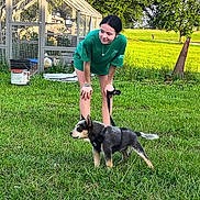 Rex is registered to the contest to win money with this photo: girl, puppy, dog, green_shirt, leash, grass, outdoor, greenhouse, garden, sunlight, smile, young_person, pet, nature, summer, casual_clothing, trees, playful, animal, field