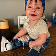 Kenley is registered to the contest to win money with this photo: baby, blue_bow, headband, smiling, jeans, ripped_jeans, white_sneakers, nike, wooden_table, indoor, cute, child, happy, casual_clothing, portrait, sitting, person, infant, fashion, footwear