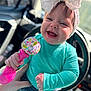 baby, child, smiling, headband, bow, rattle, toy, car_seat, car_interior, happy, cute, clothing, teal_sweater, denim_shorts, infant, portrait, hand, playful, closeup, young