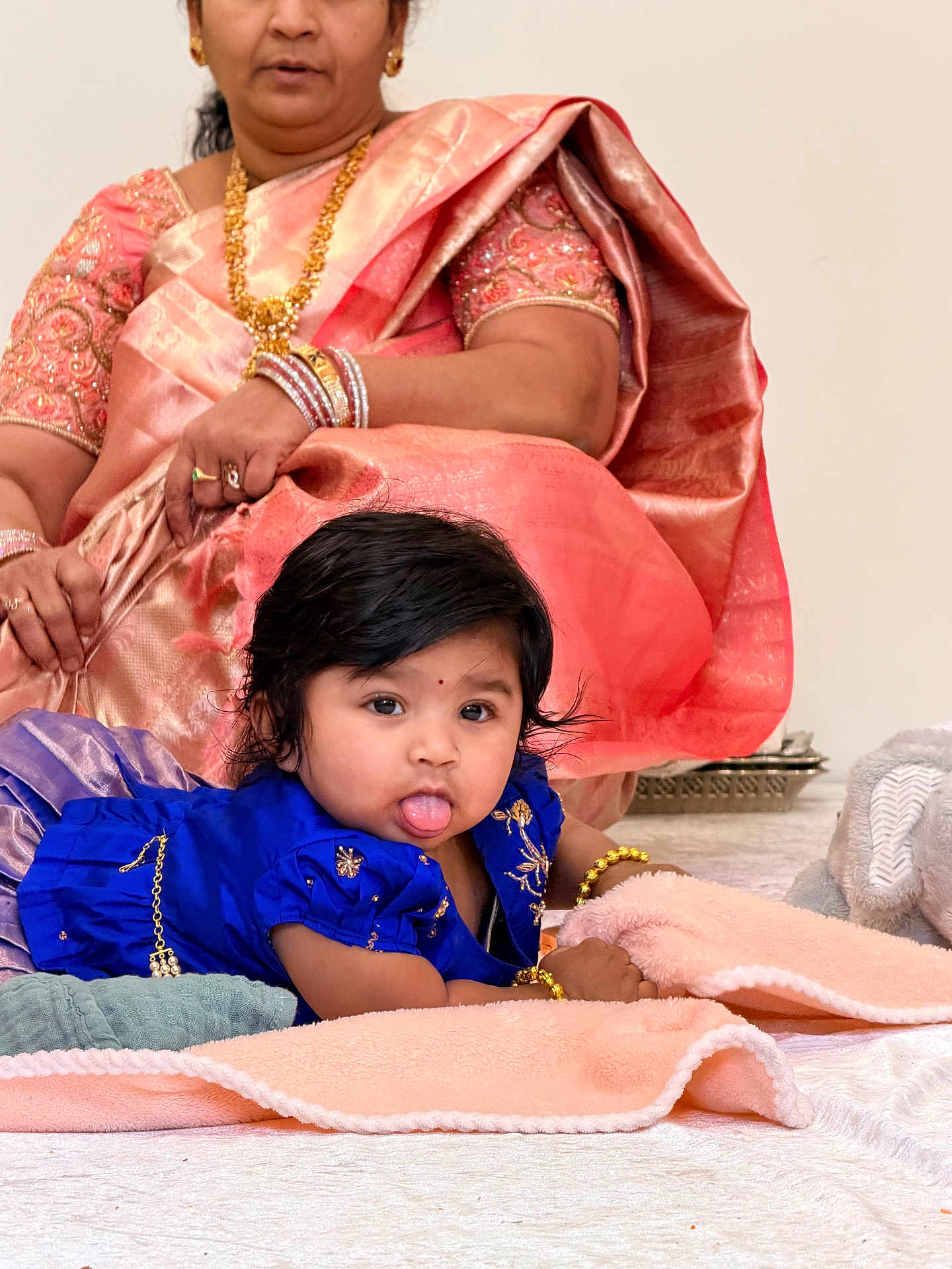 Krithya Repaka is registered to the contest to win money with this photo: baby, child, woman, saree, jewelry, blue_dress, blanket, floor, indoor, cute, tongue_out, bracelet, gold, traditional_clothing, portrait, person, infant, candid, family, soft_texture