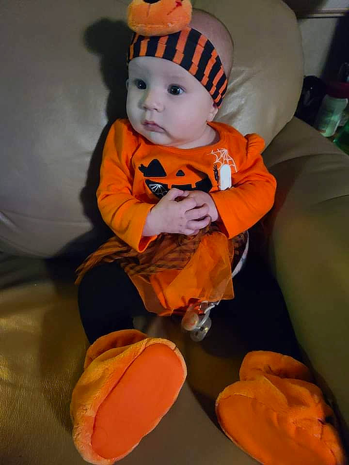 Brylee is registered to the contest to win money with this photo: baby, baby_toddler_clothing, calabaza, chair, child, costume, costume_hat, eye, fun, hat, headgear, headwear, orange, person, personal_protective_equipment, pumpkin, sitting, sports_gear, stuffed_toy, t_shirt