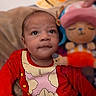 Sebastian is registered to the contest to win money with this photo: baby, child, infant, red_clothing, plush_toy, stuffed_animal, indoor, portrait, cute, curious, seated, hand, face, expression, soft_toy, colorful, young_child, looking_up, cozy, casual
