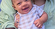 Sebastian is registered to the contest to win money with this photo: baby, smiling, infant, person, curly_hair, green_shirt, onesie, checkered_pattern, holding, close_up, happy, portrait, cute, child, affection, warmth, face, skin, arm, outdoor