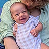 baby, smiling, infant, person, curly_hair, green_shirt, onesie, checkered_pattern, holding, close_up, happy, portrait, cute, child, affection, warmth, face, skin, arm, outdoor