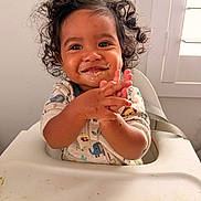 Julian is registered to the contest to win money with this photo: toddler, child, curly_hair, high_chair, messy_face, clapping_hands, smiling, indoor, baby_food, cute, happy, person, infant, apparel, long_sleeves, light_switch, window, face, skin, hands