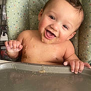 Leonidas is registered to the contest to win money with this photo: baby, child, infant, smiling, happy, laughing, high_chair, feeding, food, messy, mealtime, portrait, face, eyes, hands, indoor, chair, tray, colorful, bare_shoulders