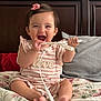 Gianna is registered to the contest to win money with this photo: baby, child, girl, smiling, happy, bed, bedspread, floral, cable, pink_bow, clothing, striped, room, pillow, wooden_headboard, cute, indoors, sitting, playful, expression
