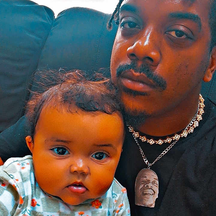 Amari joined the competition — help win amazing prizes! baby, braids, casual, child, closeup, clothing, couch, expression, face, family, holding, home, indoor, infant, man, necklace, patterned_clothing, person, portrait, sitting