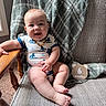 baby, infant, smiling, sitting, onesie, chair, blanket, wooden_sign, milestone, indoors, happy, person, cute, child, portrait, furniture, carpet, decor, expression, skin