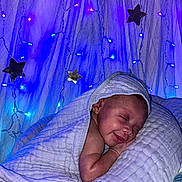 Kalyapea joined the competition — help win amazing prizes! baby, blanket, pillow, smile, sleeping, infant, face, fairy_lights, stars, blue_lights, purple_lights, soft_texture, cozy, cute, resting, indoors, newborn, peaceful, wrapped, decor