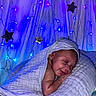baby, blanket, pillow, smile, sleeping, infant, face, fairy_lights, stars, blue_lights, purple_lights, soft_texture, cozy, cute, resting, indoors, newborn, peaceful, wrapped, decor