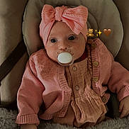 Nina participe au concours pour gagner de l'argent avec cette photo : baby, infant, pacifier, headband, pink_clothing, cardigan, blanket, seat, cushion, hand, cute, child, indoors, cozy, soft_texture, portrait, newborn, warm, comfortable, adorable
